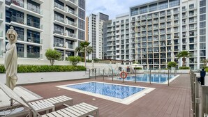 A rooftop pool area with lounge chairs, a statue, and modern apartment buildings in the background. - Sophisticated Studio Getaway, Minutes Drive to Iconic Dubai Landmarks - Azizi Riviera 45, Al Merkadh (Dubai)