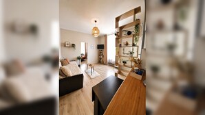 Un salon moderne avec un canapé, une table basse et un téléviseur. On y trouve une bibliothèque agrémentée de plantes et d’objets décoratifs.