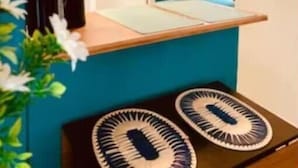 Une pièce aux murs de couleur turquoise, avec un comptoir en bois, un luminaire suspendu et une vue sur une cuisine par le biais d’une fenêtre.