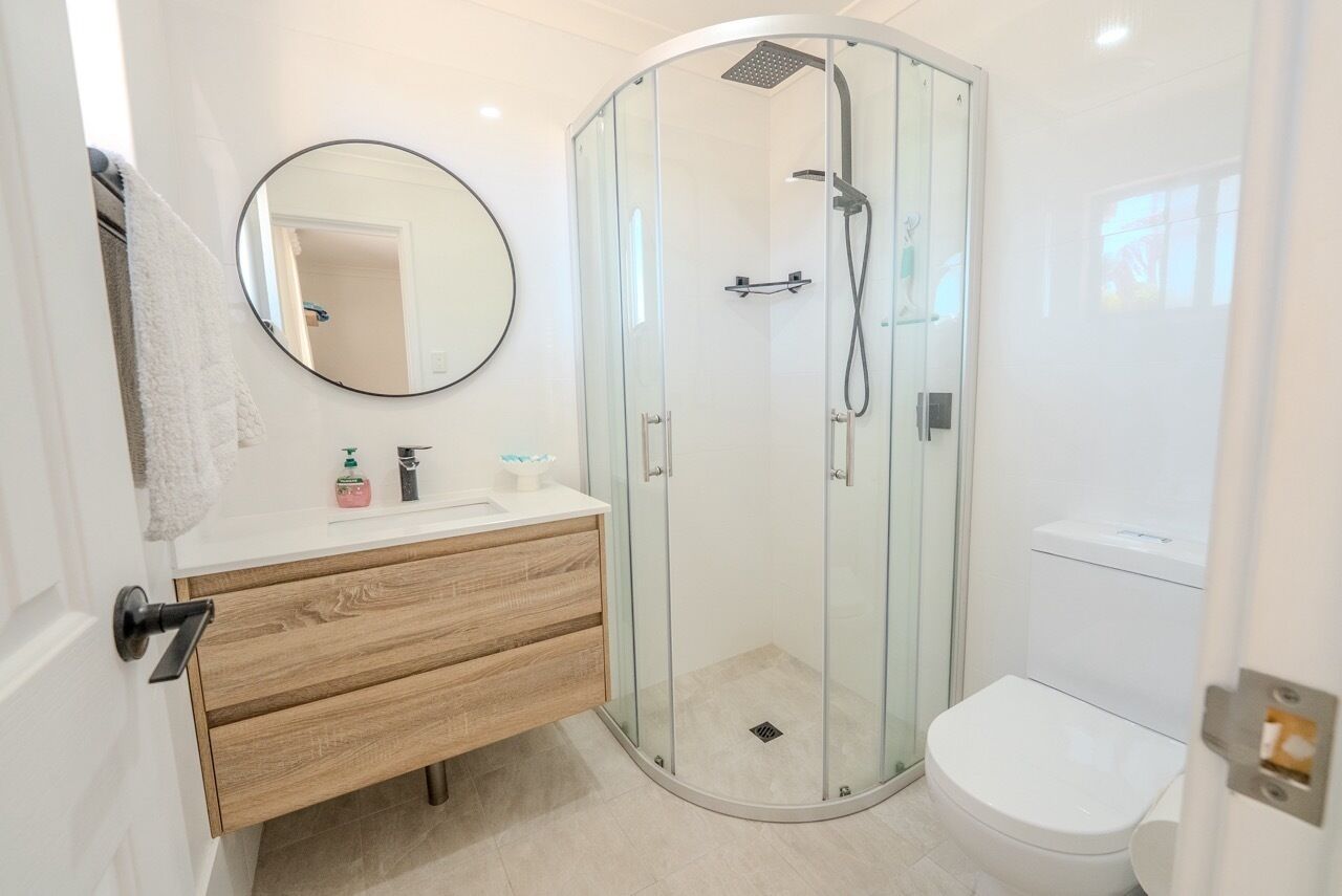 Un baño moderno con cabina de ducha de vidrio, inodoro y tocador con espejo.