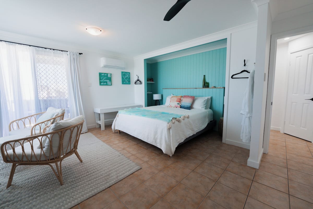 A bedroom with a bed, a chair, a bedside table, and a window with curtains.