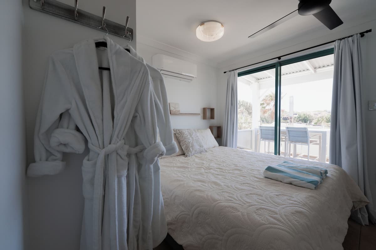 A bedroom with a bed, a robe hanging on the wall, and a view of the outdoors through a large window.