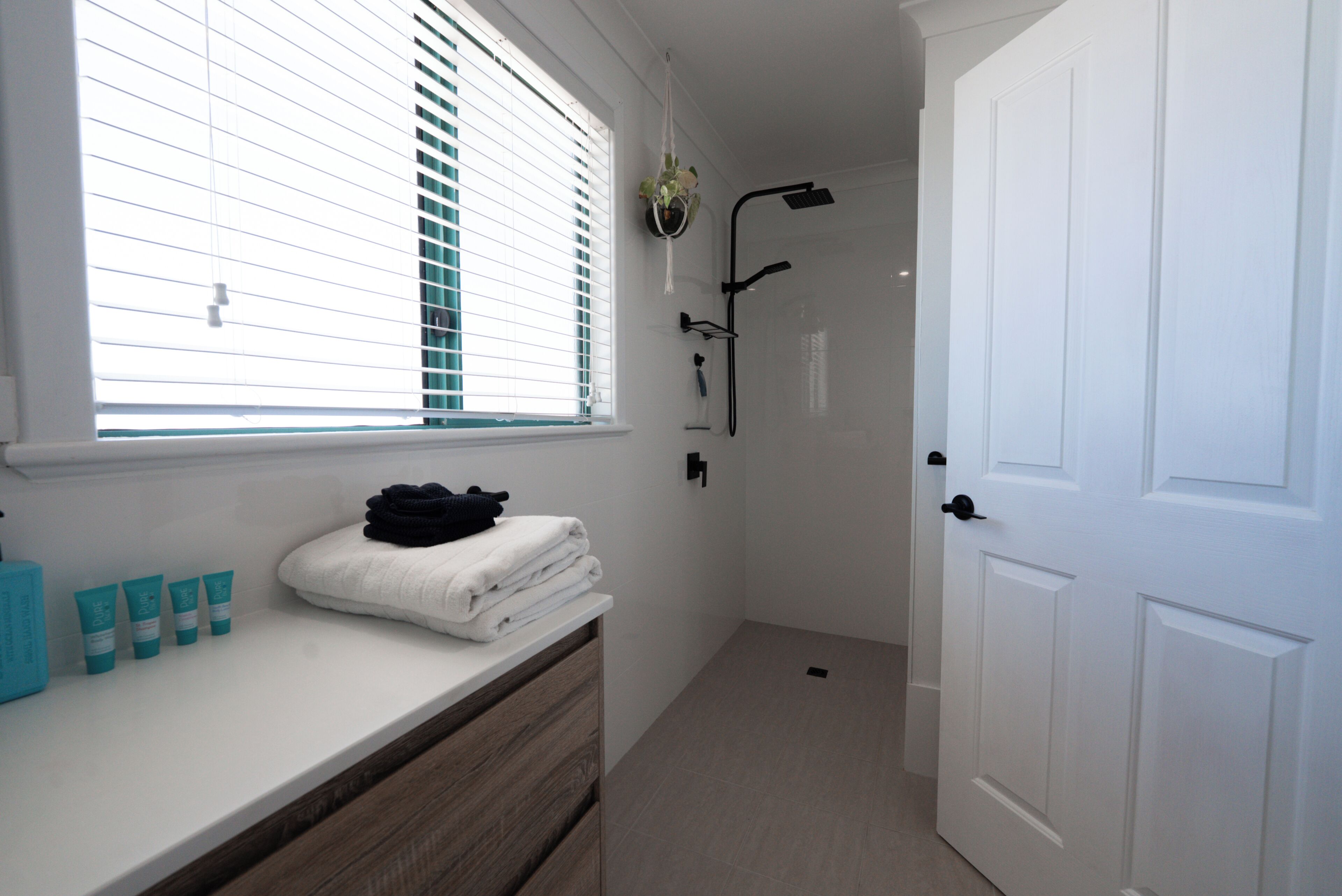 A bathroom with a window, a shower, a towel rack, and a vanity with toiletries.