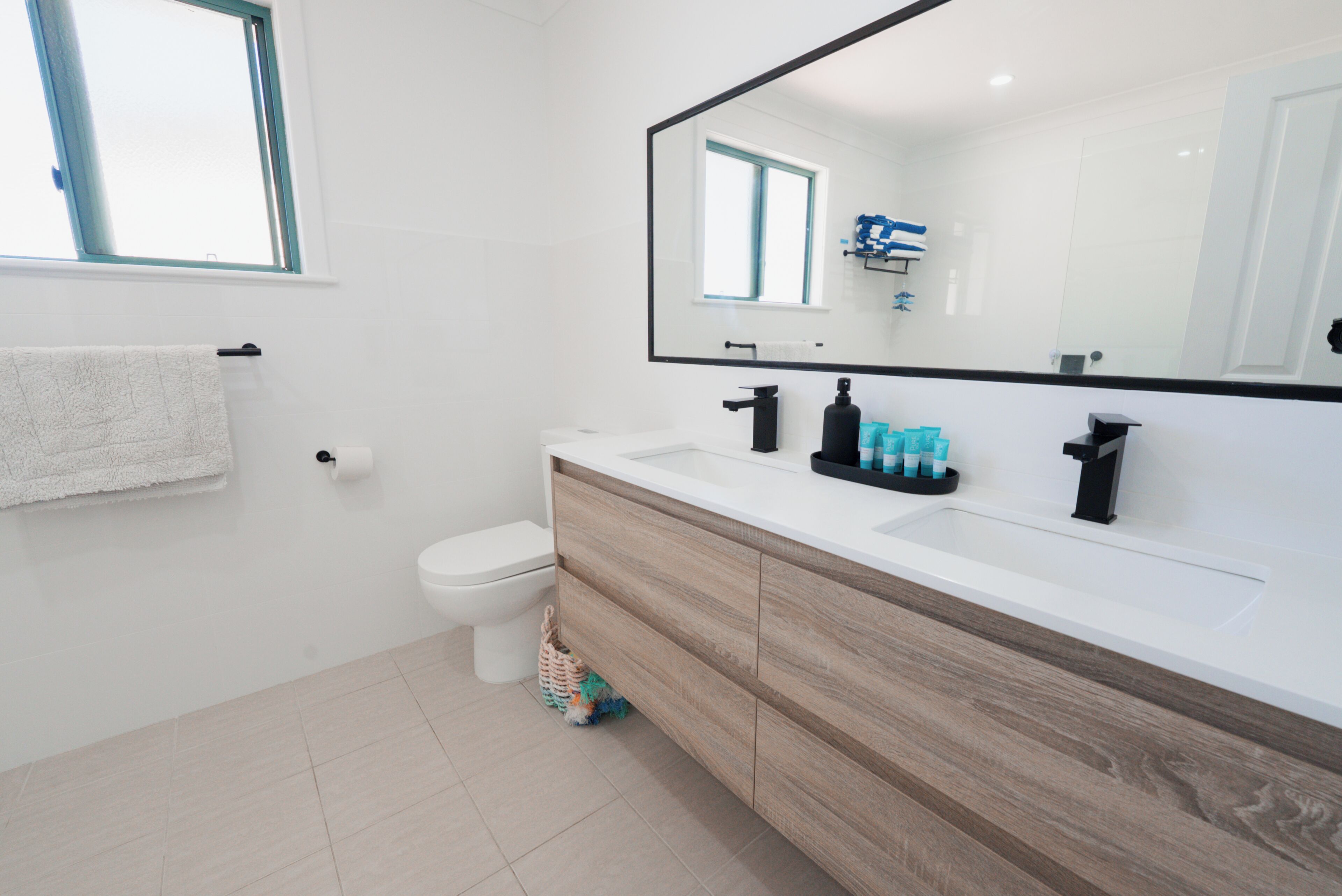 Un baño moderno con inodoro blanco, tocador de madera, espejo grande y ventana.