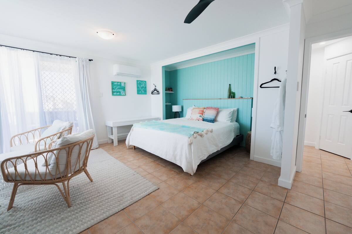 A bedroom with a bed, a chair, a bedside table, and a bathroom door.