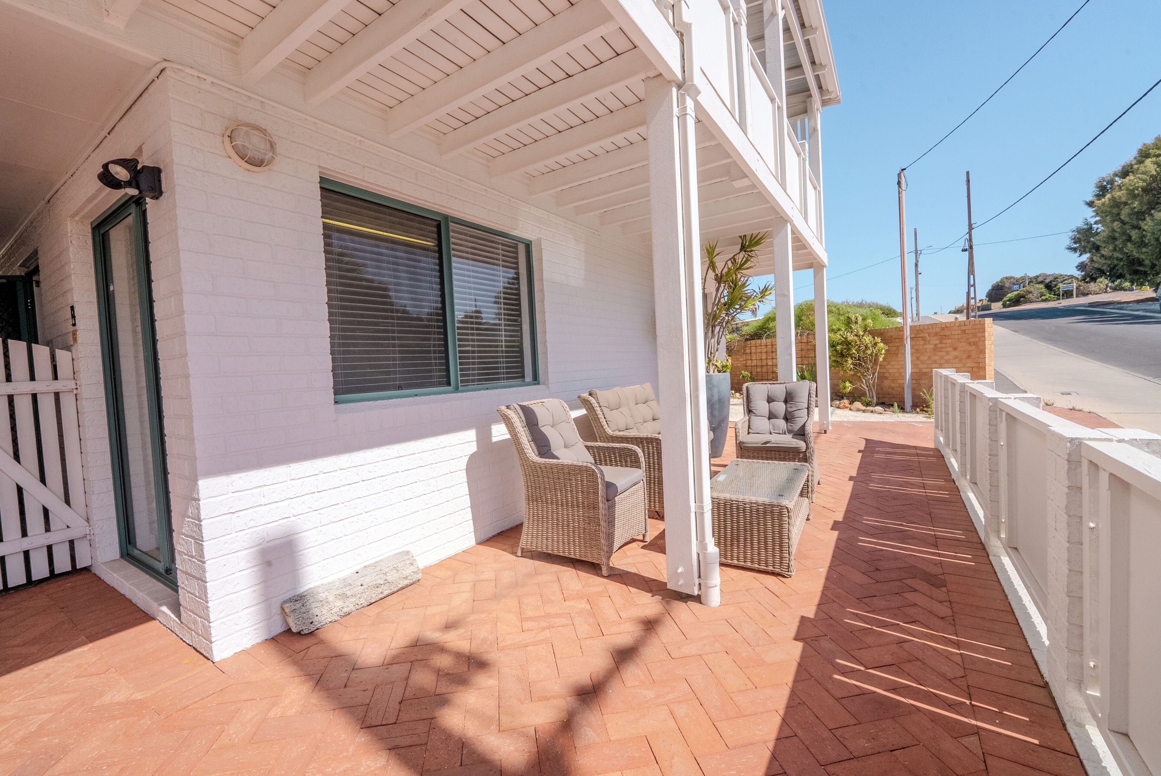 A white building with a covered patio, wicker furniture, and a brick floor.
