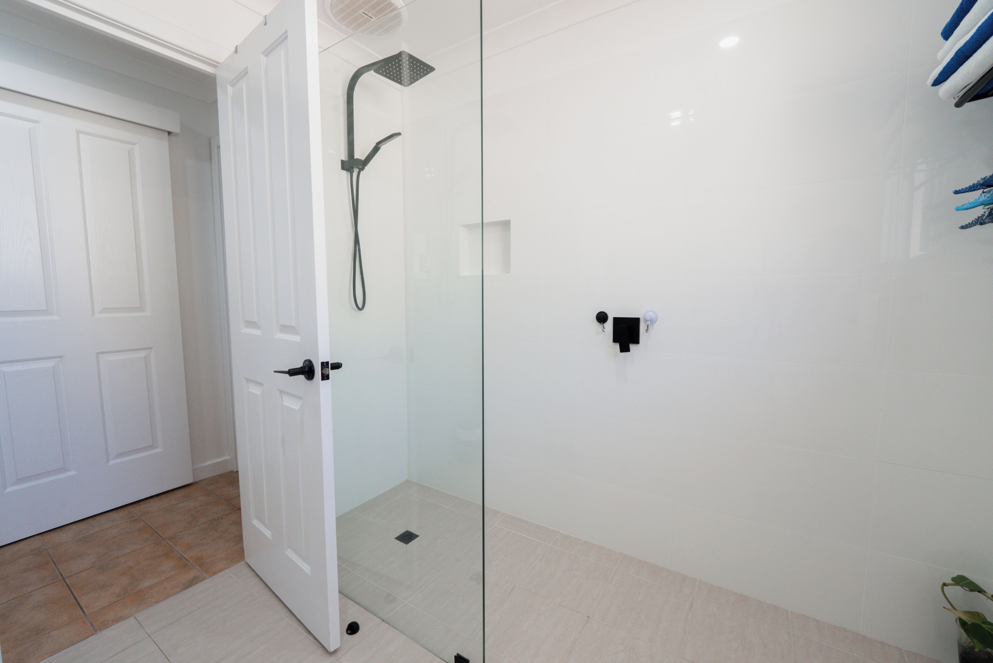 Une salle de bain avec une douche à parois de verre, une porte blanche et un sol carrelé.