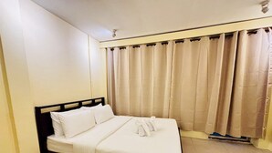 A single bed with white bedding in a room with beige walls and curtains. - Sukhum Charoen Krung Tak-Sin guest house (Bangkok)