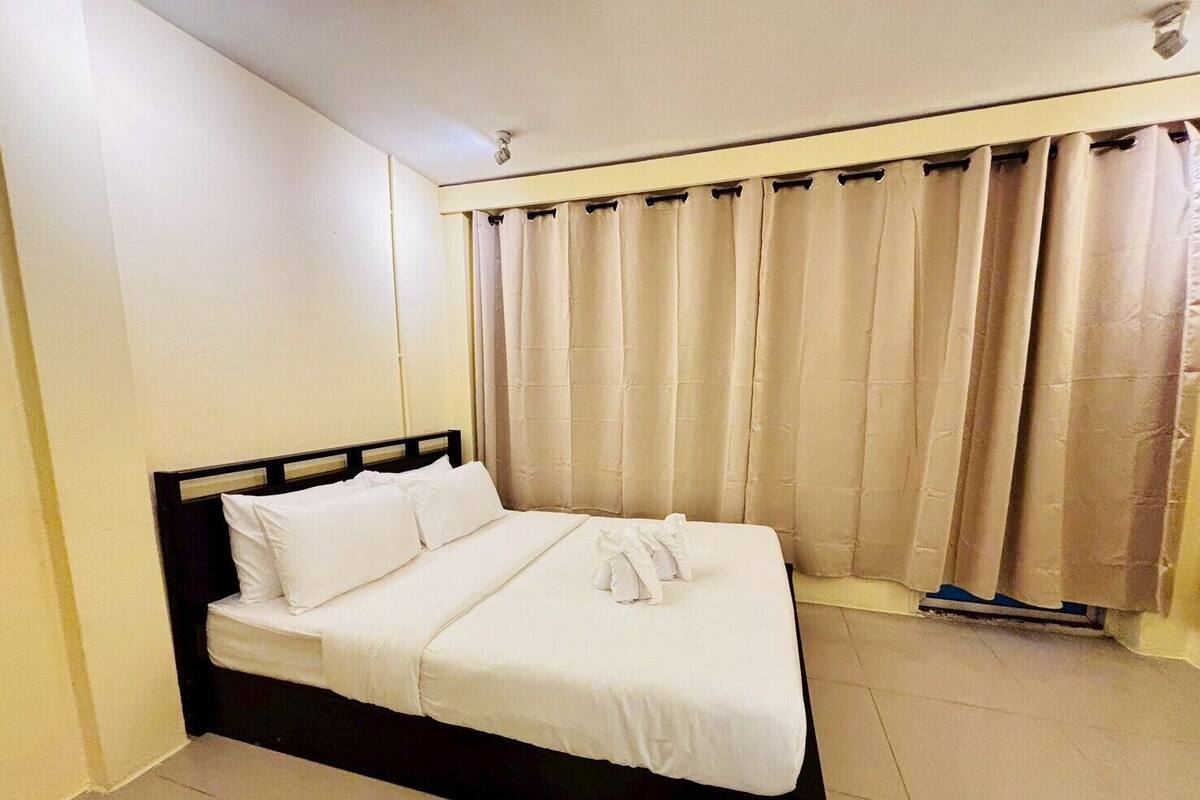 A single bed with white bedding in a room with beige walls and curtains.