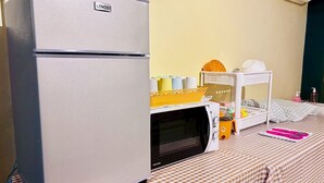 A compact kitchenette with a refrigerator, microwave, and a small table with a checkered tablecloth. - Sukhum Charoen Krung Tak-Sin guest house (Bangkok)
