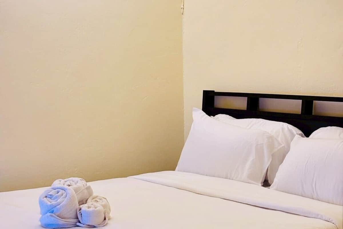 A bed with white linens and pillows, a headboard, and a wall with a visible crack.
