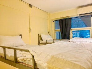 Ein Krankenzimmer mit zwei Betten, einem Fenster mit Vorhängen, einer Klimaanlage und einer Wandsteckdose.