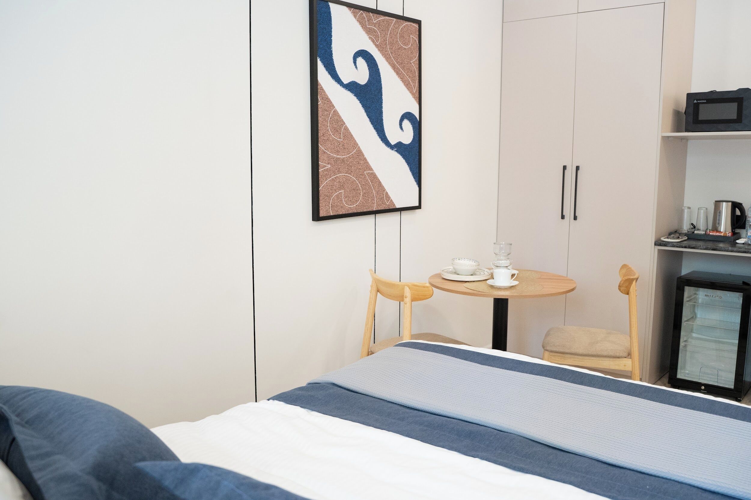 Habitación de hotel con cama, una mesita con taza y plato, microondas y refrigerador.