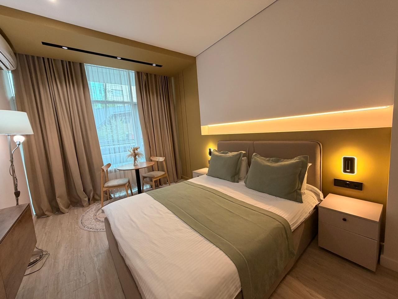 Ein Hotelzimmer mit einem großen Bett, Nachttischen, einem Schreibtisch mit Stuhl und einem Fenster mit Vorhängen.