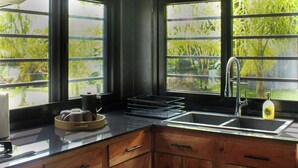 Cozinha com armários de madeira, pia e janela com vista para o verde.