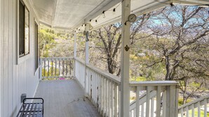 A covered porch with a bench, a clock, and a view of trees and hills. - Mtn-View Getaway w/ Game Room, 1 Mi to Kern River! (Wofford Heights)