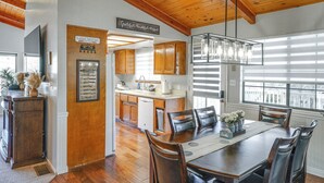 A dining area with a wooden table, chairs, and a chandelier. There is a kitchen in the background with wooden cabinets and a dishwasher. - Mtn-View Getaway w/ Game Room, 1 Mi to Kern River! (Wofford Heights)
