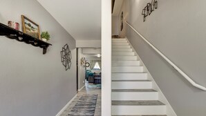 Un pasillo con una escalera, una repisa con adornos y una alfombra.