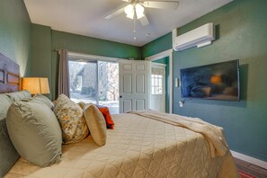 A bedroom with a bed, a ceiling fan, a TV, and a door leading outside.