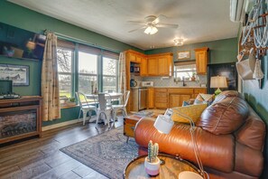 A living room with a leather sofa, a dining table with chairs, a fireplace, and a kitchen area with wooden cabinets and appliances.