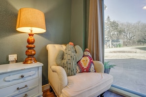 A room with a white sofa, a lamp, a dresser, and a view of a street through a window.