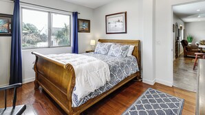 Ein Schlafzimmer mit einem hölzernen Bett, einem Fenster mit Vorhängen, einem Deckenventilator und gerahmten Bildern an der Wand.