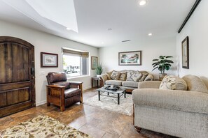 Una sala de estar con un sillón de cuero marrón, un sofá color beige, una mesa de centro y un ventanal grande.