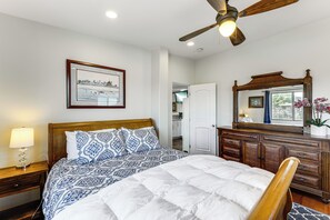 Un dormitorio con cama, cabecera de madera, mesita de noche, cómoda y espejo, además de ventilador de techo.