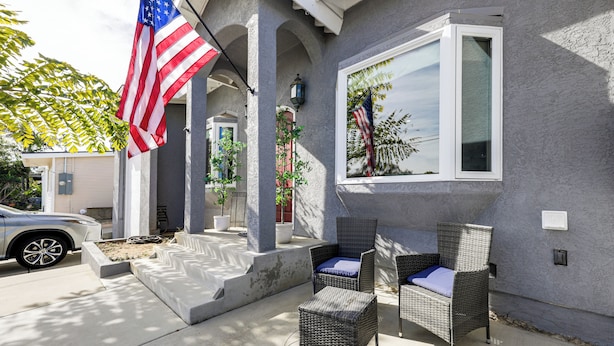 Ein Haus mit einer Veranda, zwei Korbstühle mit Kissen, einer amerikanischen Flagge und einem Fenster mit Blick auf eine Landschaft.