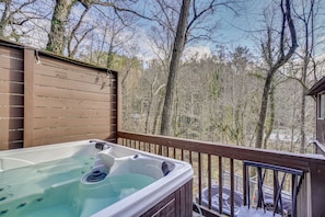 Un jacuzzi en una terraza de madera con vista a árboles sin hojas y un cielo despejado.