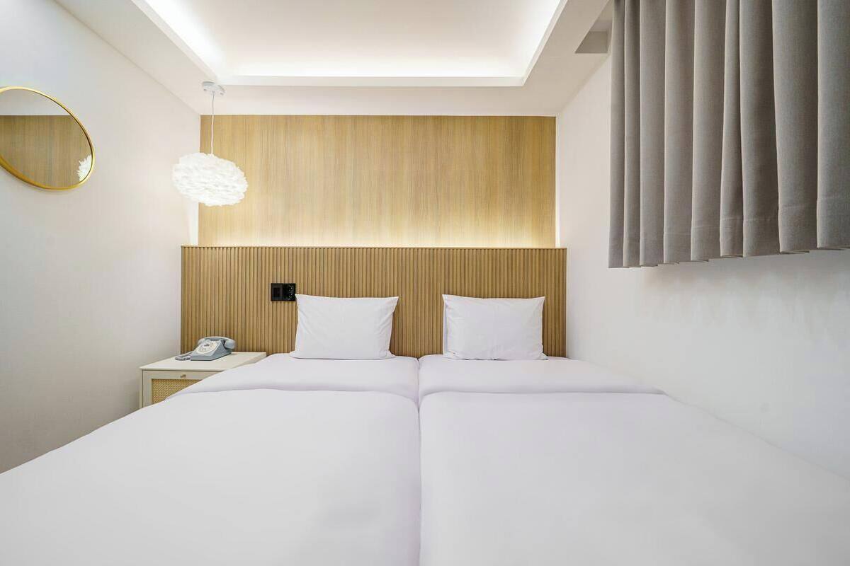 Une chambre d’hôtel avec un grand lit, une table de chevet avec un téléphone, un miroir fixé au mur et un luminaire au plafond.