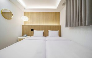 Hotellihuone, jossa on suuri sänky, yöpöytä, jossa on puhelin, seinälle kiinnitetty peili ja kattovalaisin.