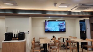 A modern dining area with tables and chairs, a flat-screen TV mounted on the wall, and a coffee station with dispensers. - Hotel Stay Yeoyu (Seoul)