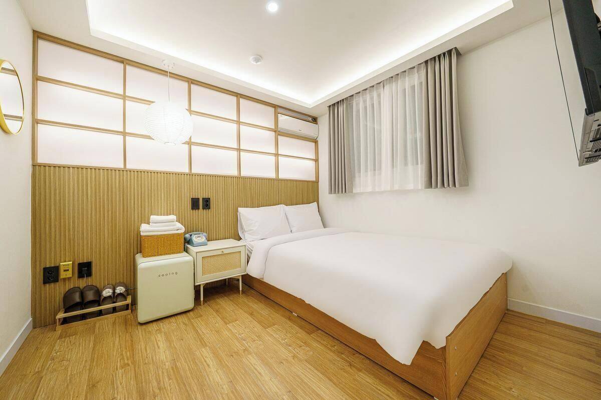 Une chambre d’hôtel moderne avec une tête de lit en bois, un lit, une petite table de chevet, une commode, un miroir et un luminaire au plafond.