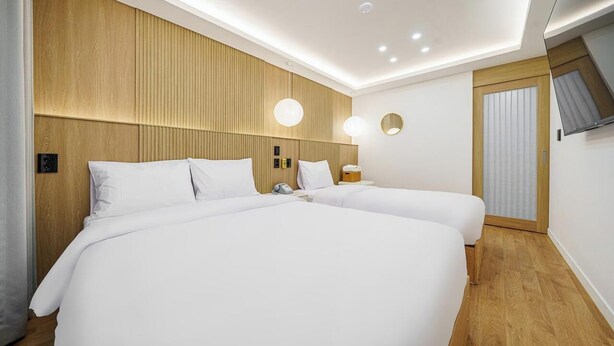 A hotel room with two beds, wooden headboard, recessed ceiling lights, bedside tables, and a TV mounted on the wall. - Hotel Stay Yeoyu (Seoul)