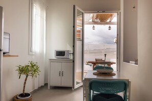 Ein Zimmer mit einem Esstisch, Stühlen, einer Topfpflanze, einer Mikrowelle und einer Schiebetür zu einem Außenbereich.