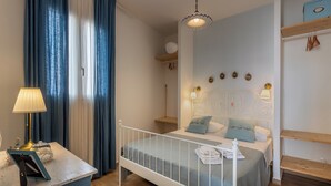 Una camera da letto con un letto bianco, un comodino con una lampada, una finestra con tende blu e una parete decorata con piatti.