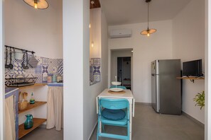 A compact kitchen with a dining table, a chair, a refrigerator, and a TV. - Marinella Seafront (Avola)
