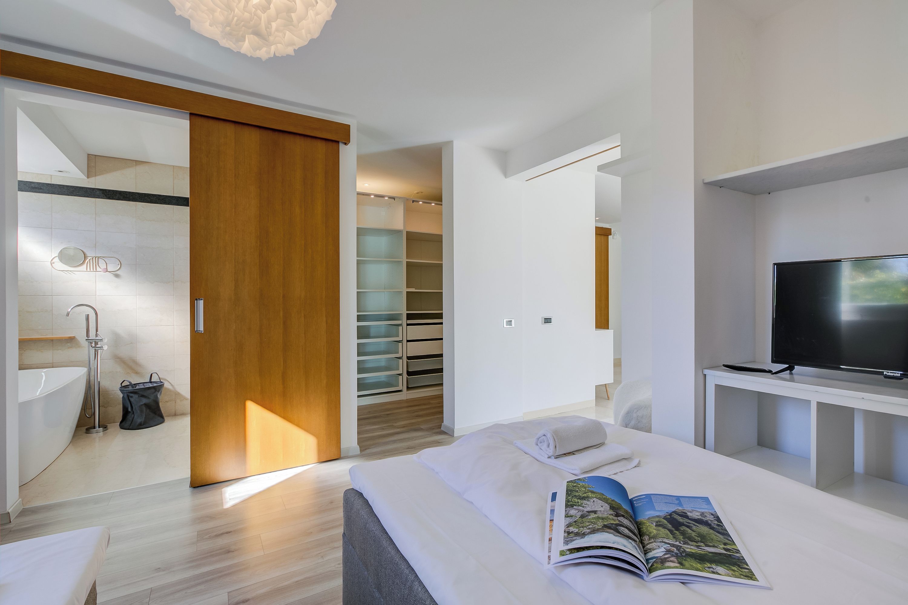 Una habitación de hotel moderna con una cama grande, televisión, baño con bañera y vestidor.