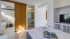 Una habitación de hotel moderna con una cama grande, televisión, baño con bañera y vestidor.
