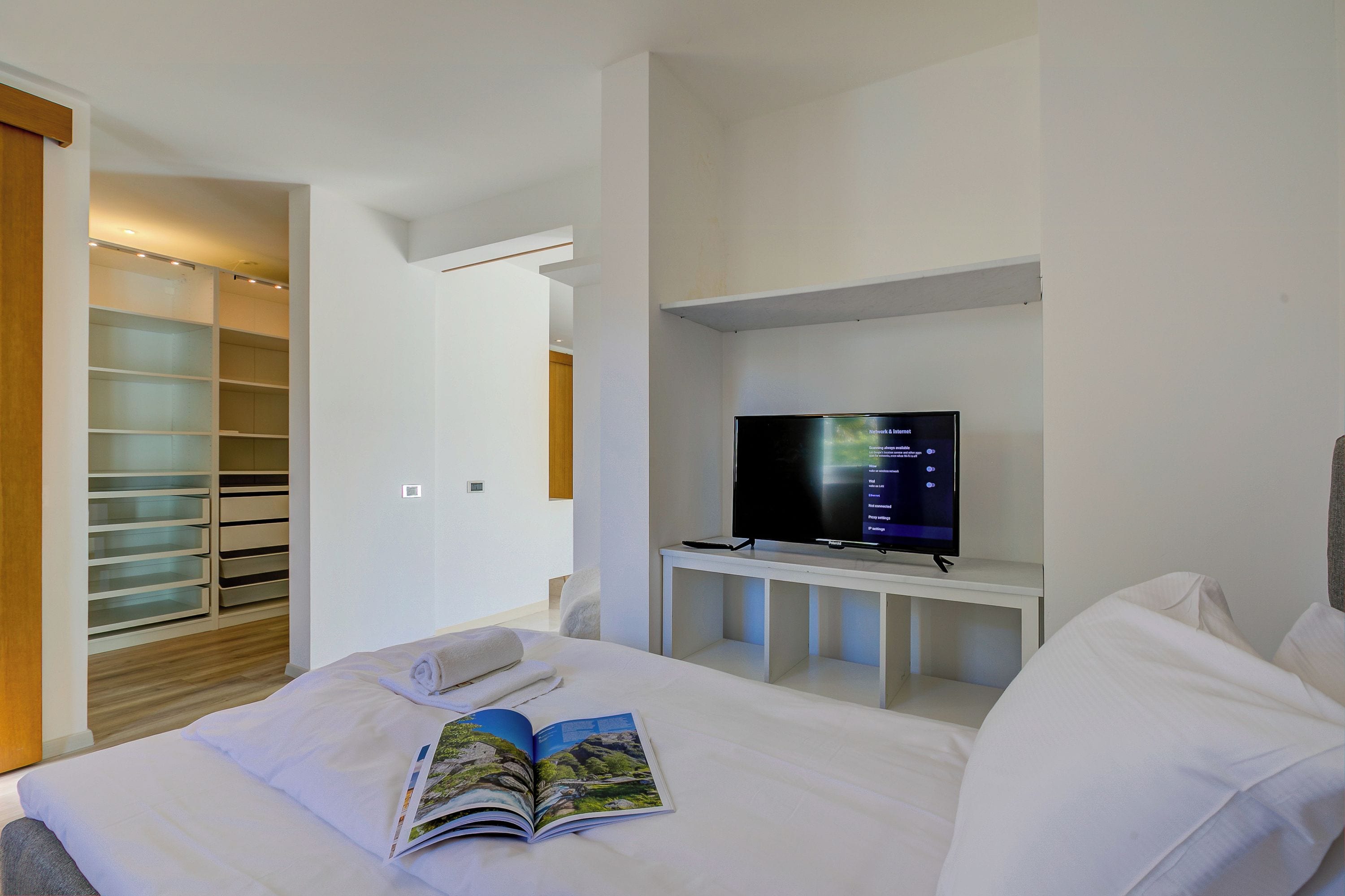 A hotel room with a bed, a TV on a stand, a bookshelf, and a walk-in closet.