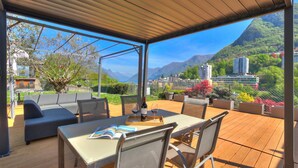 Un patio al aire libre con una mesa, sillas y un sofá, con vistas a un paisaje montañoso.