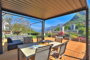 An outdoor patio with a table, chairs, and a sofa, overlooking a mountainous landscape. - Lugano Lake View Villa w. Private Pool (Lugano)