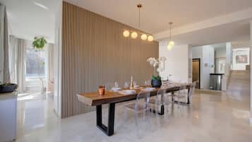 A modern dining area with a long wooden table, clear chairs, and a vertical wooden panel.