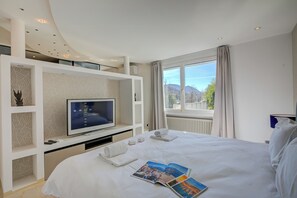 Une chambre d’hôtel avec un lit, une télévision, une fenêtre donnant sur un beau paysage et un balcon.
