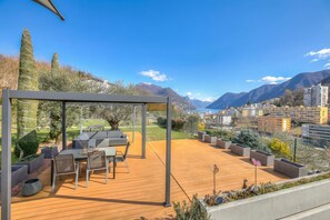 Une terrasse en bois, dotée de mobilier d’extérieur, d’une pergola et offrant une vue sur les montagnes et la ville.