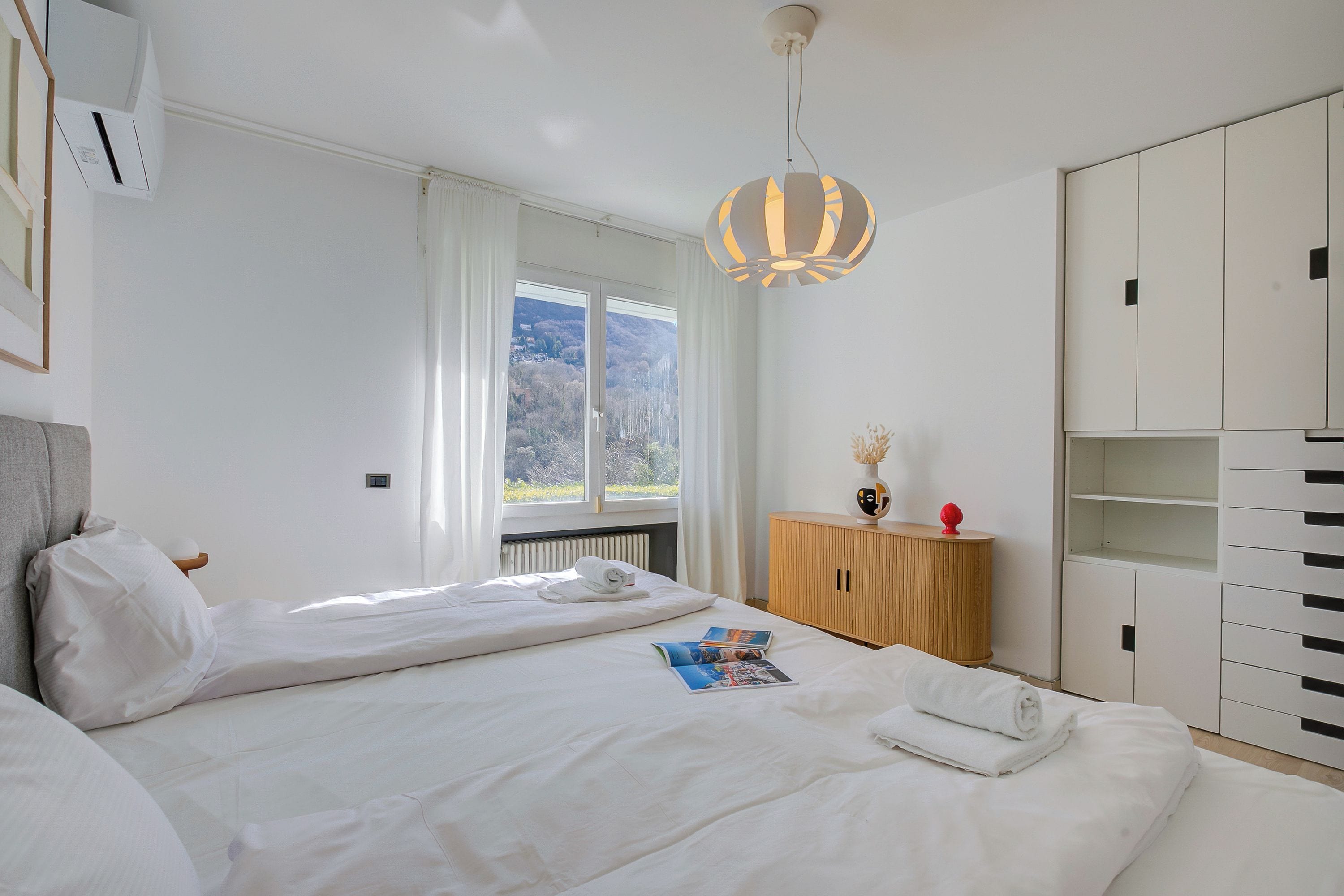 A bedroom with a bed, a window, a wardrobe, and a bedside table.