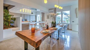 Una cocina moderna con una larga mesa de madera, sillas transparentes y vistas al exterior.