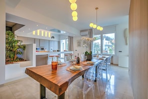 A modern kitchen with a long wooden table, clear chairs, and a view to the outside. - Lugano Lake View Villa w. Private Pool (Lugano)
