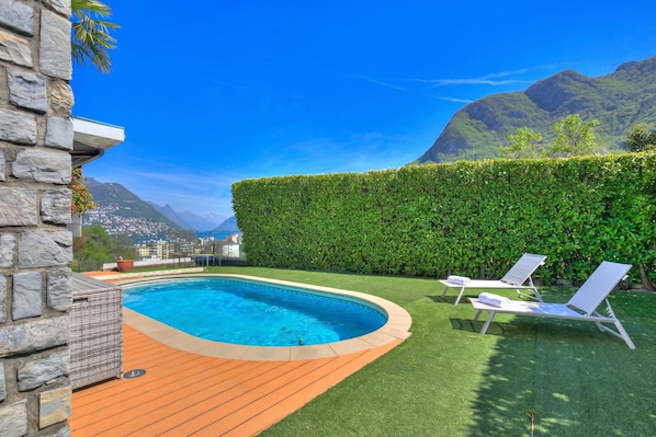 A swimming pool with a wooden deck, two lounge chairs, and a hedge. - Lugano Lake View Villa w. Private Pool (Lugano)